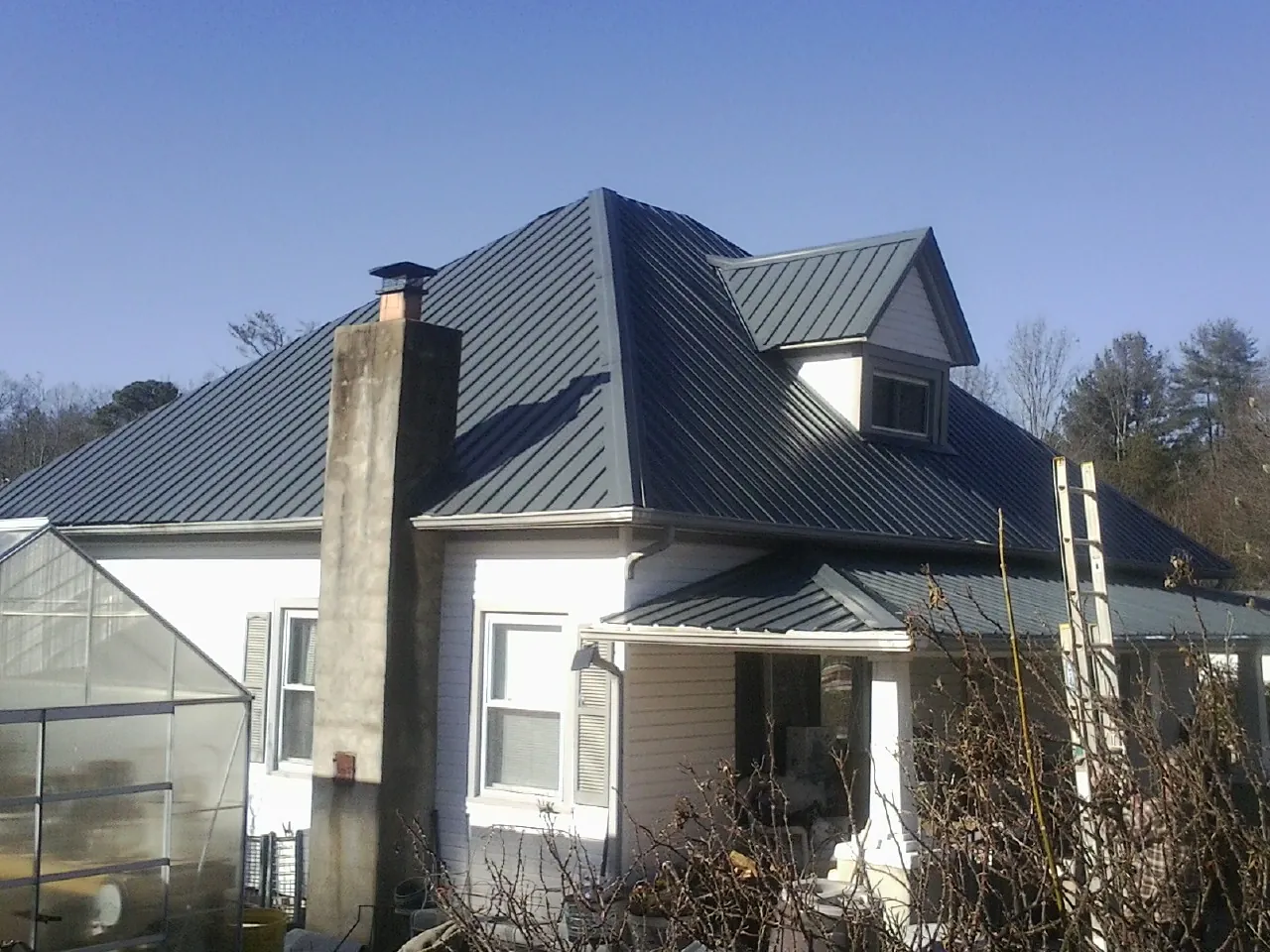 Dark blue standing seam metal roof on a white farmhouse with dormer — Slate & Tile Roof Repair by Roofing Brothers in Saint Georges