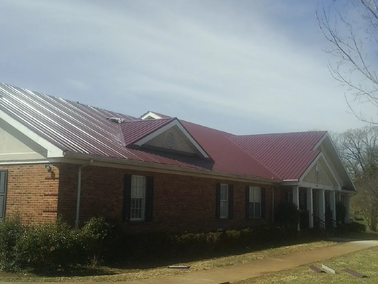 Red metal roof with gabled entries on a long brick building, from a Hail Damage Roof Repair job in Saint Georges