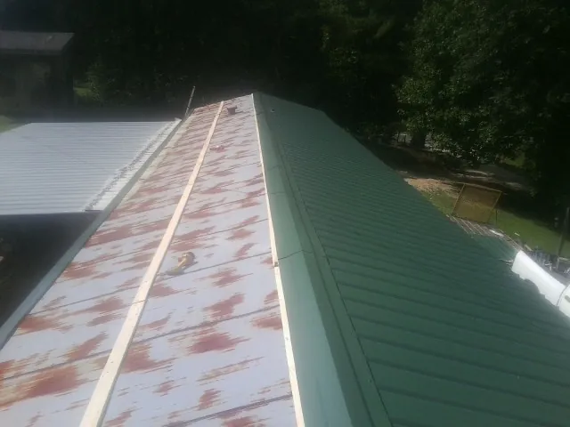 Old rusted panels beside newly installed green metal roofing — Wind Damage Roof Repair by Roofing Brothers in Saint Georges