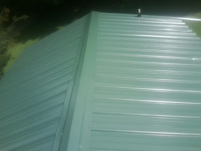 New green metal panels meeting at the ridge of a roof — Flat Roof Repair work by our crew in Saint Georges