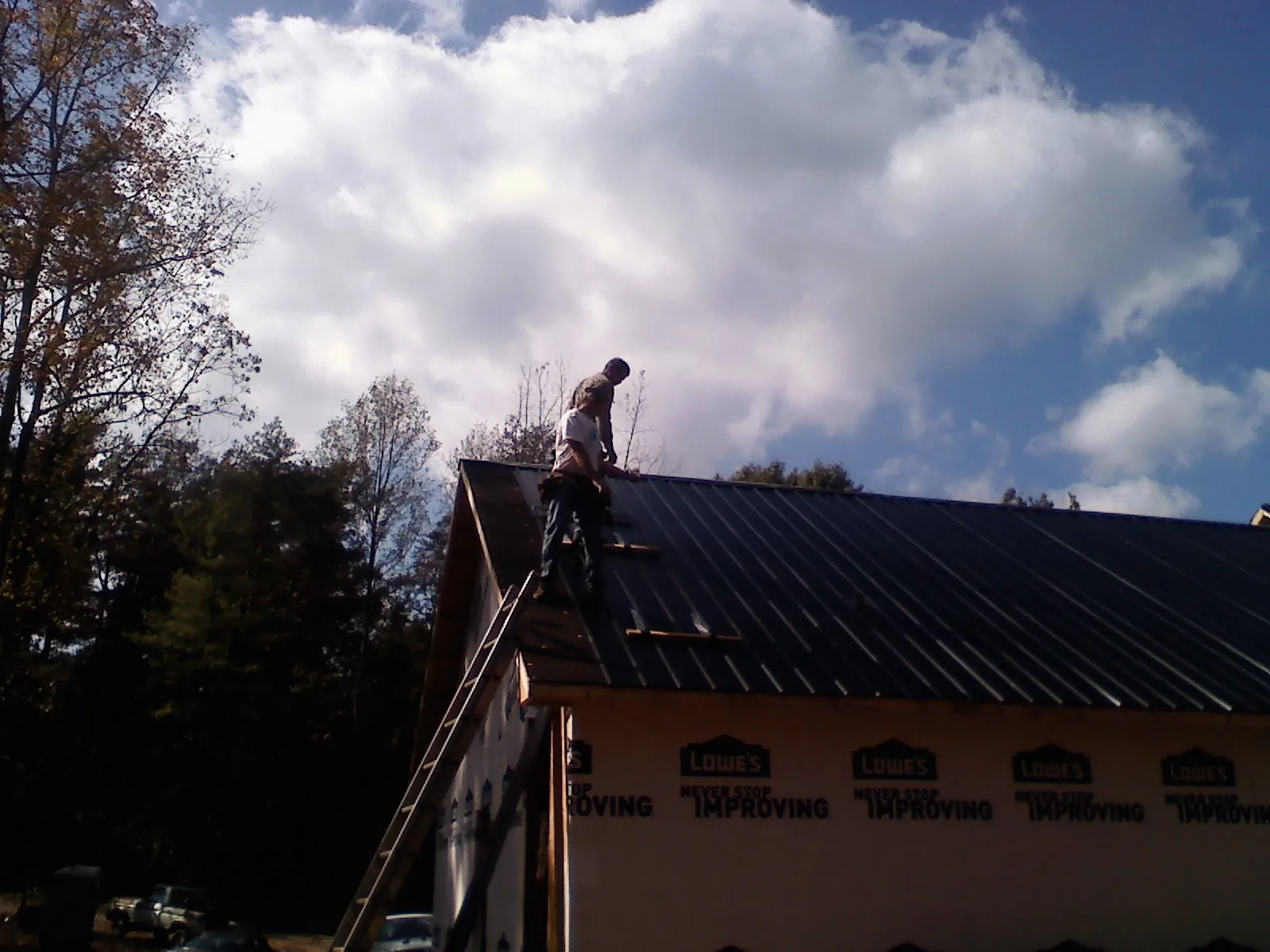 Roofer fastening dark metal panels high against a cloudy sky, from a Roof Inspection job in Saint Georges