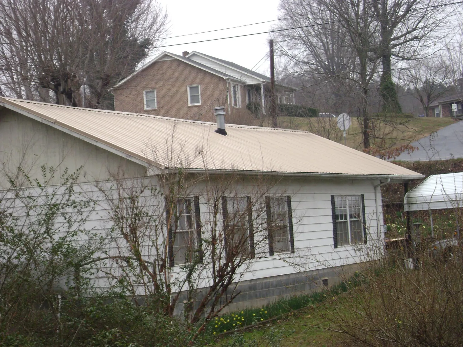 Tan metal roof on a white sided house set into a hillside — Commercial Roofing by Roofing Brothers in Saint Georges