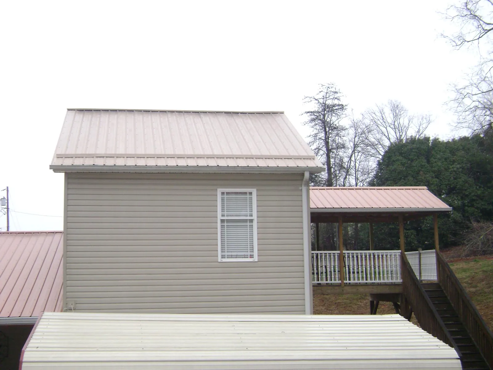 Tan metal roofs on a two story addition and attached porch, from a Roof Replacement job in Saint Georges